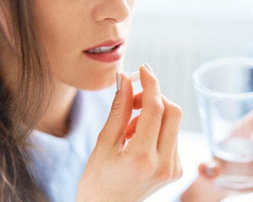 Nahaufnahme junge Frau, die eine Tablette einnimmt und ein Glas Wasser in der anderen Hand hält