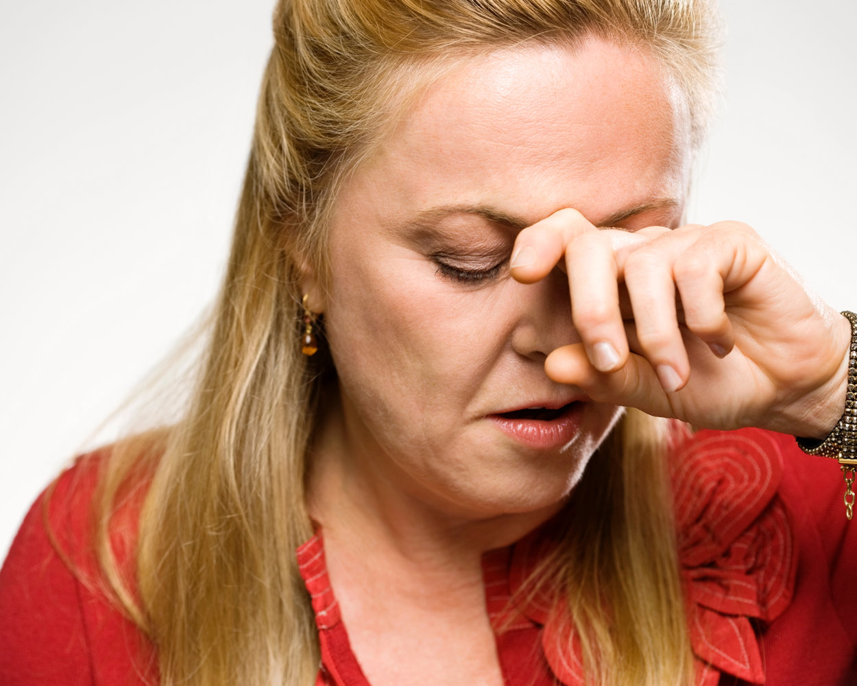 Blonde Frau die sich mit den Fingern auf die Stirn drückt, weil sie Migräne mit Übelkeit hat